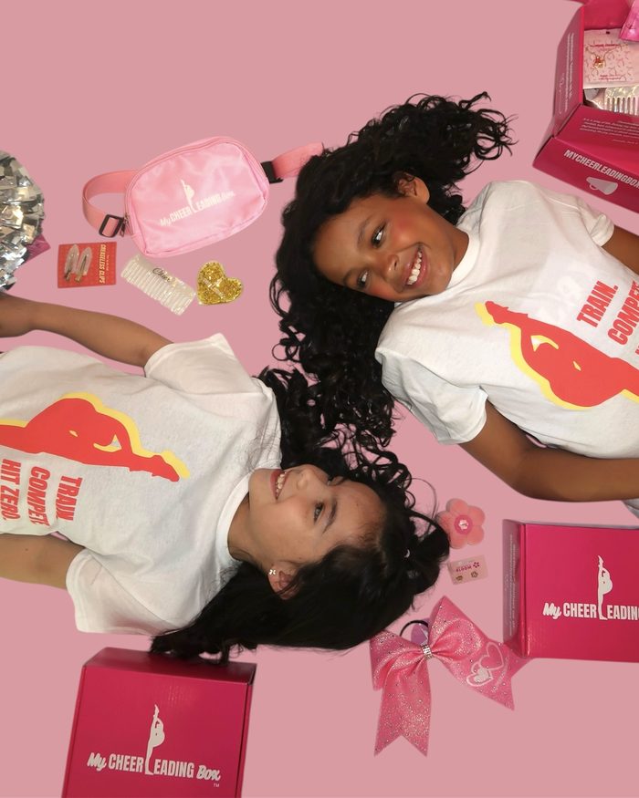 Two cheerleaders with a MyCheerleadingBox bow and box contents