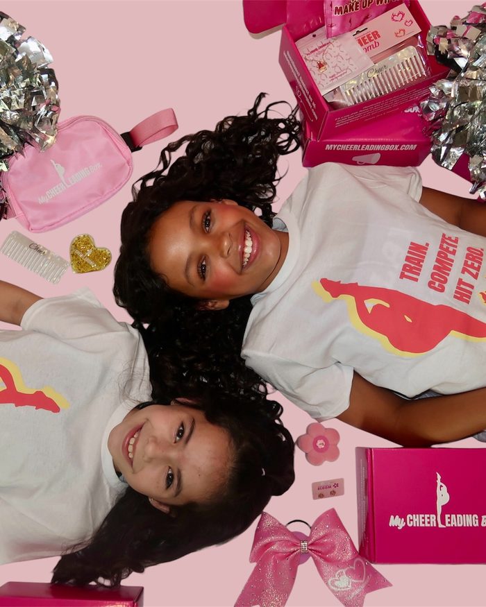 Two cheerleaders in Train Compete Hit Zero tees with pom poms and their box contents