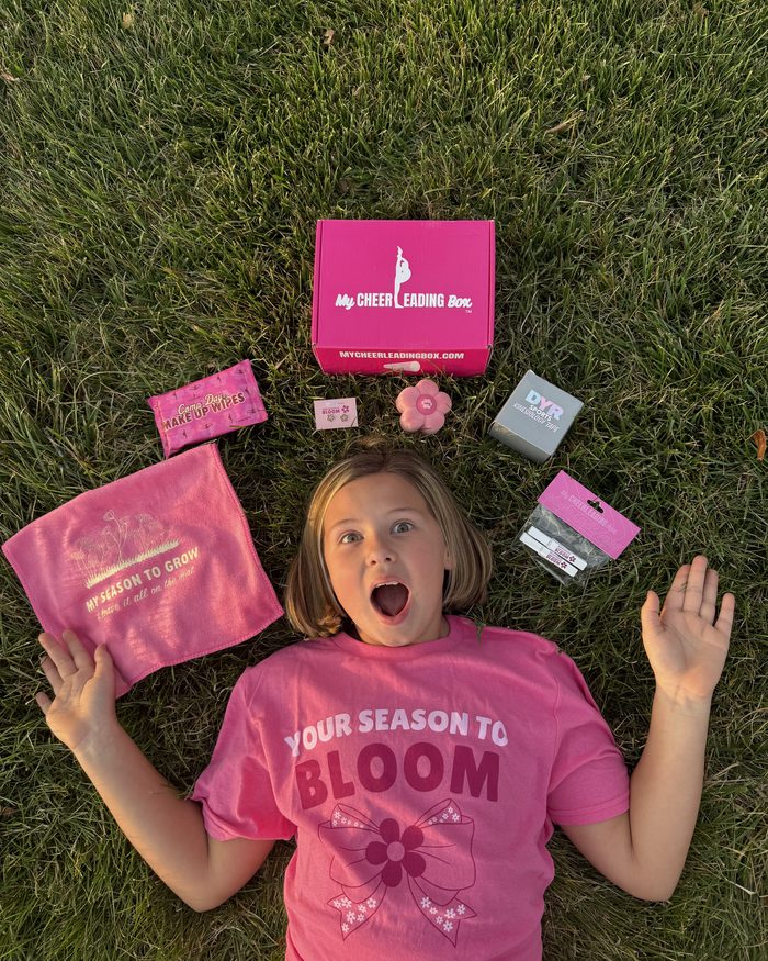 A cheerleader in the grass in her Your Season to Bloom tee with her box