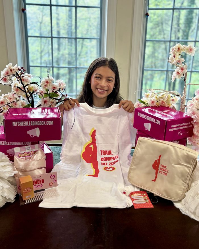 A cheerleader holding up her MyCheerleadingBox tee with the rest of her box