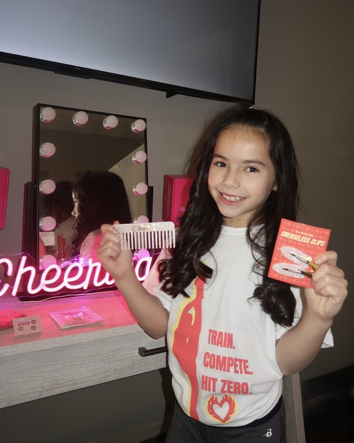 A cheerleader at her lit vanity with cheer products from her box